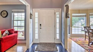 A hallway with a white door, a red couch, a dining table with chairs, and a patterned rug. - Martinez Retreat w/ Seasonal Pool: 9 Mi to Masters (Grovetown)