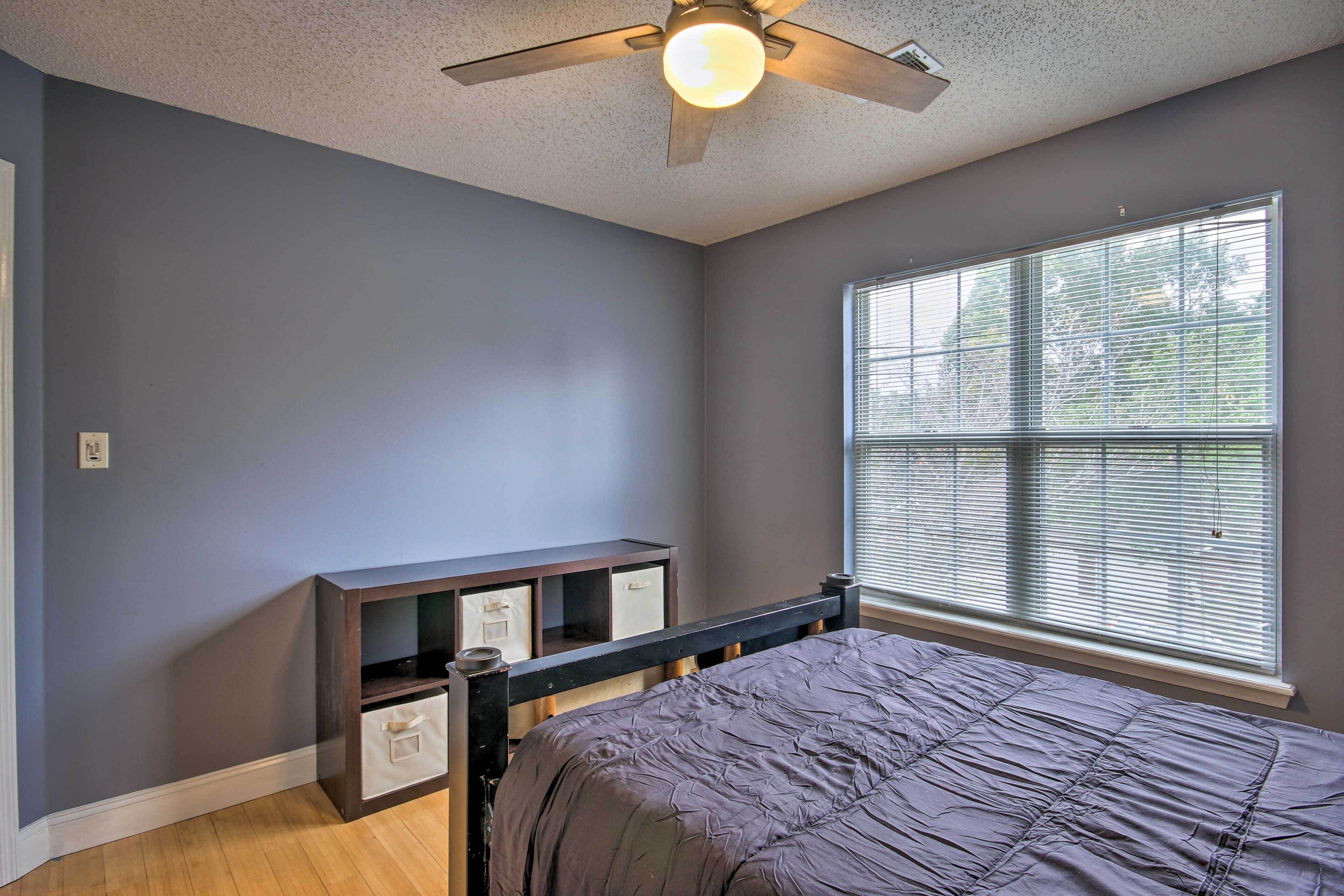 A bedroom with a bed, a ceiling fan, a window with blinds, and a nightstand with drawers.