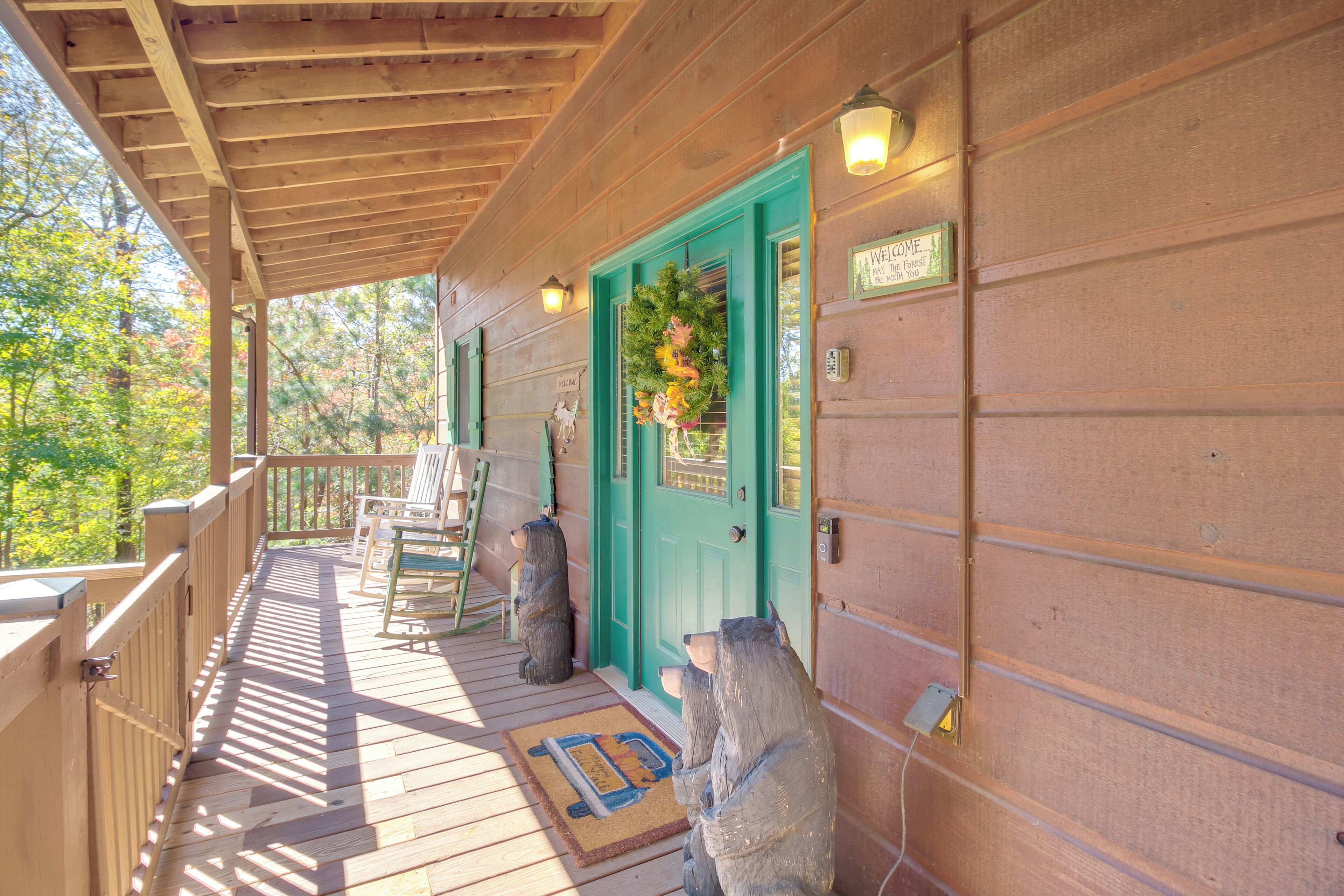 A wooden porch with a green door, a welcome sign, and two bear statues.