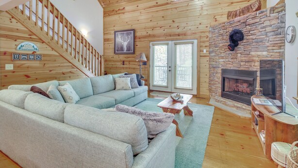 A cozy living room with a light blue sectional sofa, a stone fireplace, a wooden staircase, and a large window. - Coosawattee River Resort Home Mins From Blue Ridge (Ellijay)
