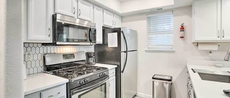 A modern kitchen with white cabinets, stainless steel appliances, a microwave, a gas stove, and a refrigerator.