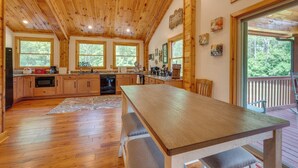 Une cuisine spacieuse avec des meubles en bois, une grande table en bois et une vue sur l’extérieur grâce à de grandes fenêtres.