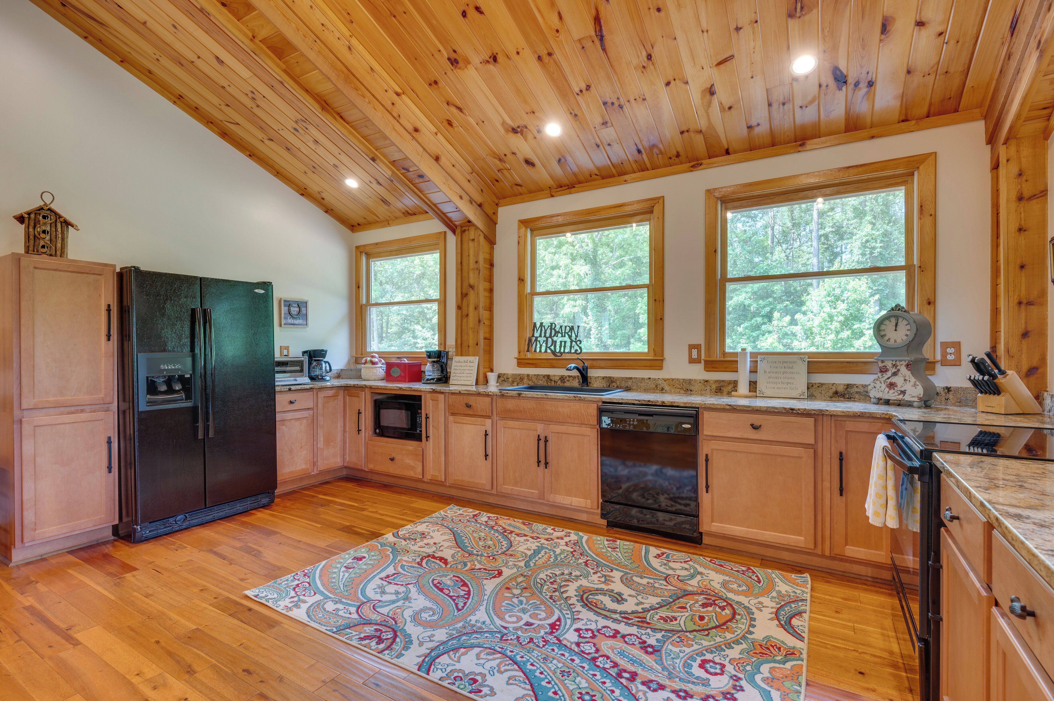 A kitchen with wooden cabinets, a refrigerator, a dishwasher, and a window with a view of trees.