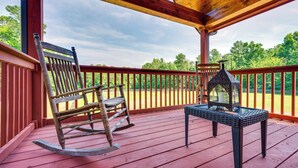 Une terrasse en bois avec un fauteuil à bascule et une table sur laquelle est posée une lanterne.