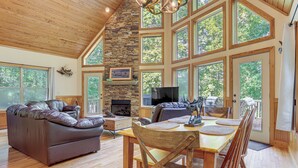 A spacious living room with a stone fireplace, large windows, and a dining area with wooden furniture. - Murrayville Lakefront Cabin w/ Boat Slip & Grill! (Murrayville)