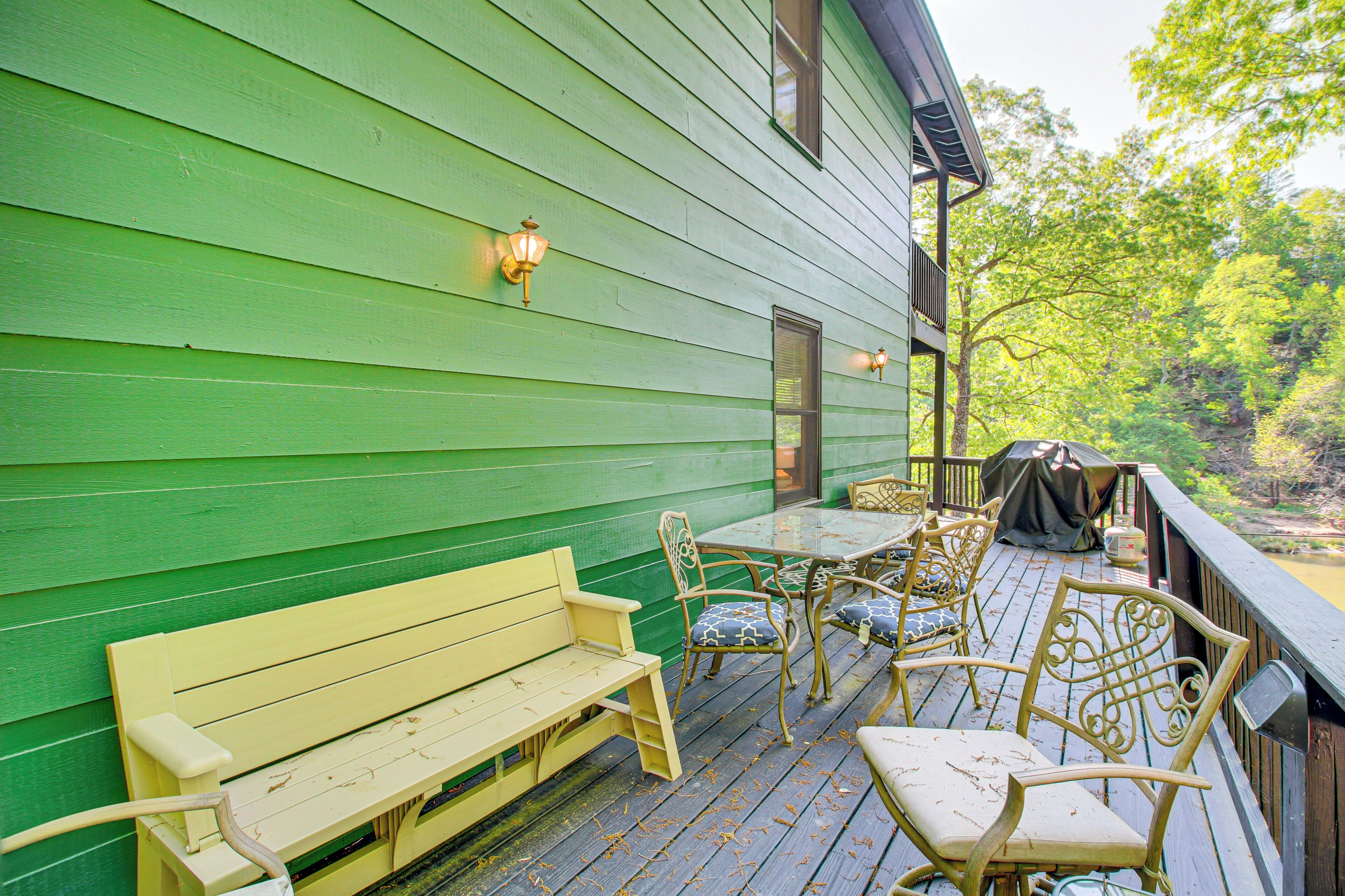 Una terraza de madera verde con un banco, sillas, una mesa y una zona cubierta.