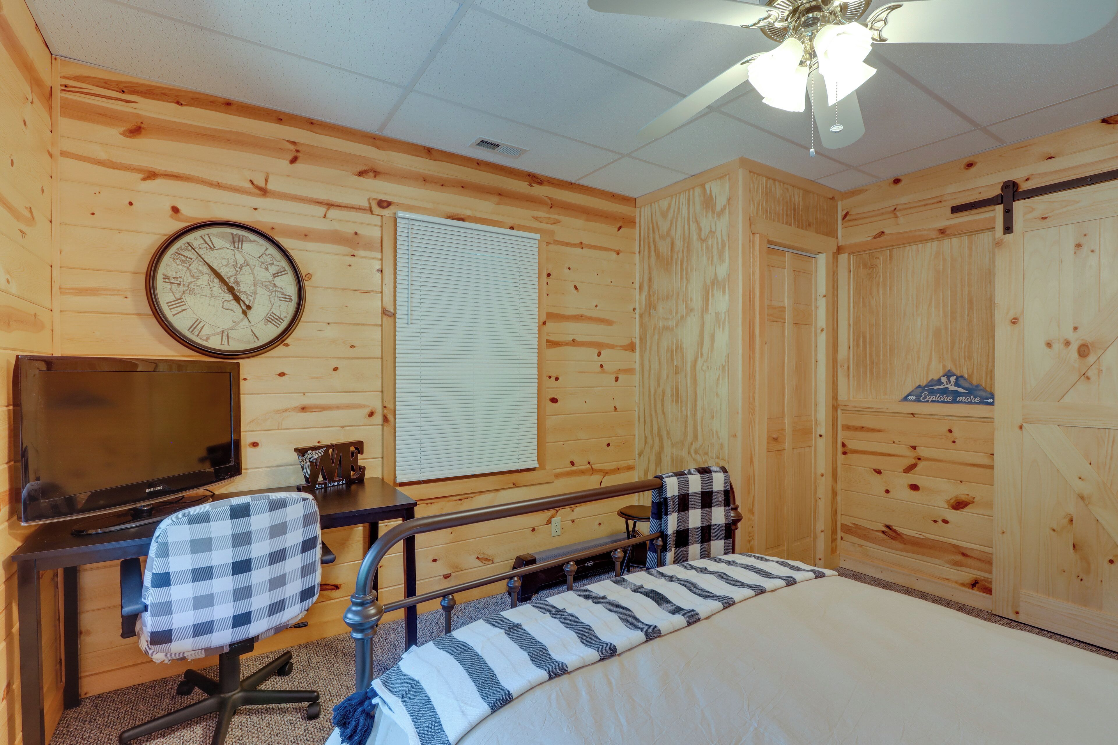 A wooden room with a bed, a desk, a chair, a television, and a clock.