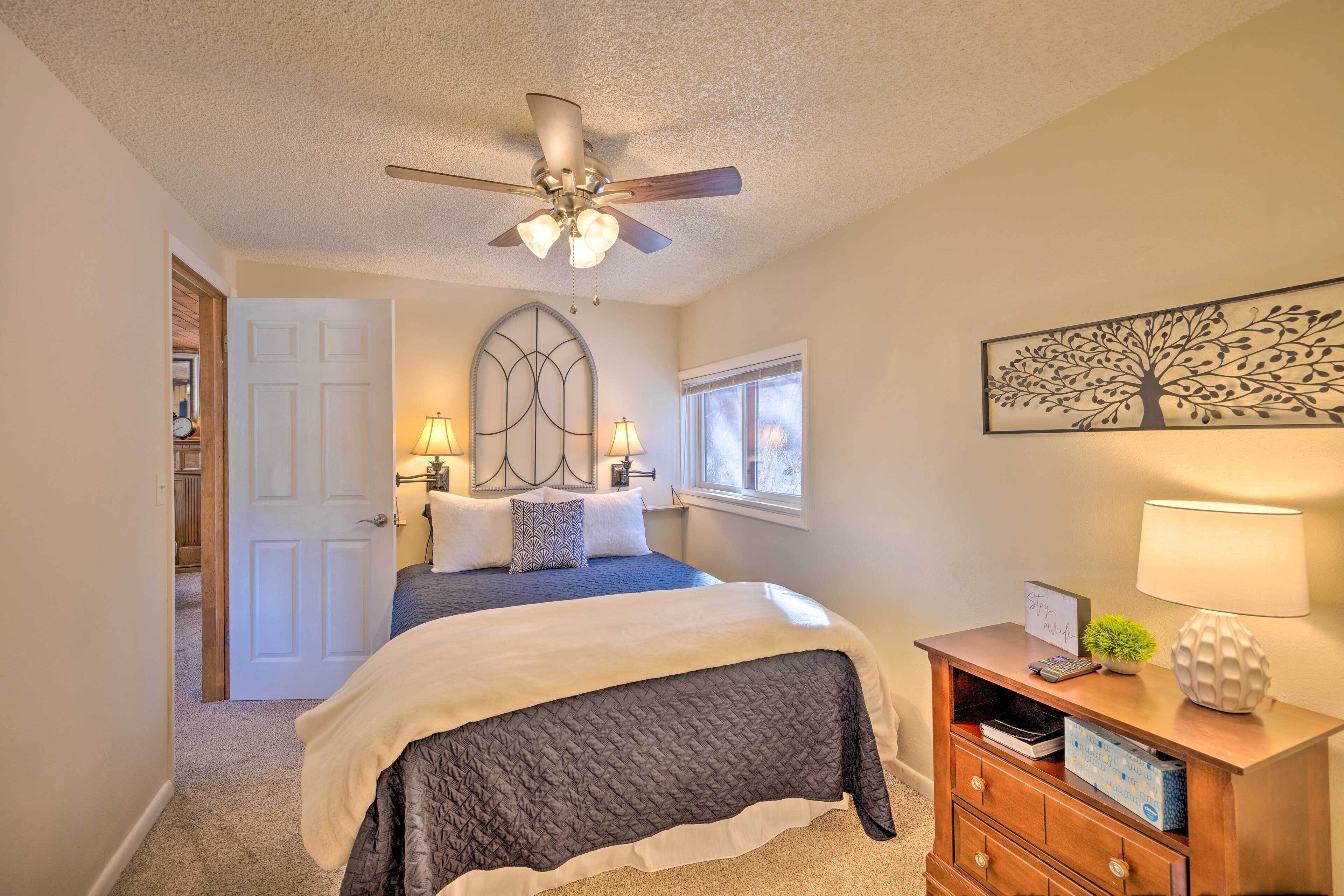 A bedroom with a bed, a ceiling fan, a nightstand with a lamp, and a wall-mounted artwork.