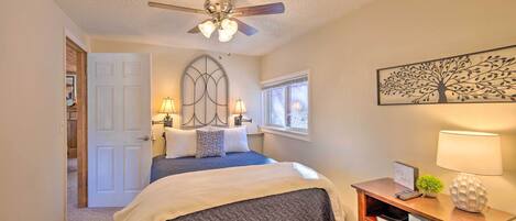 A bedroom with a bed, a ceiling fan, a nightstand with a lamp, and a wall-mounted artwork.
