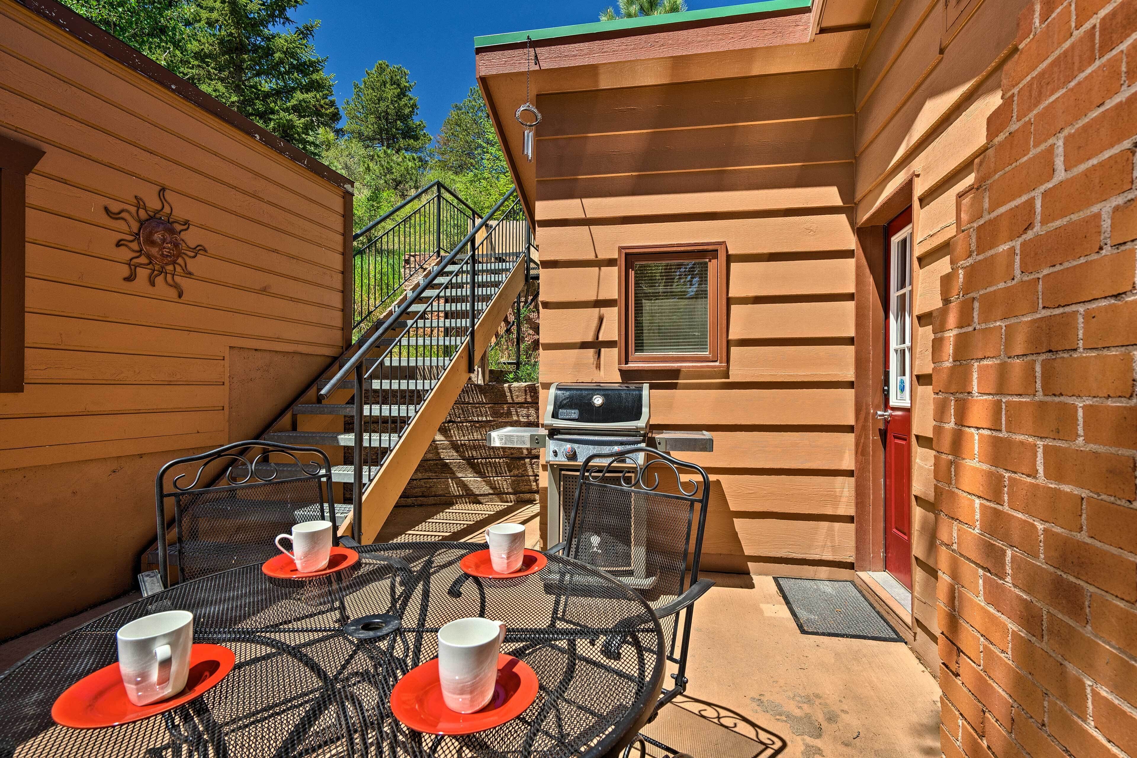A patio with a table set for two, a grill, and a staircase leading to an upper level.