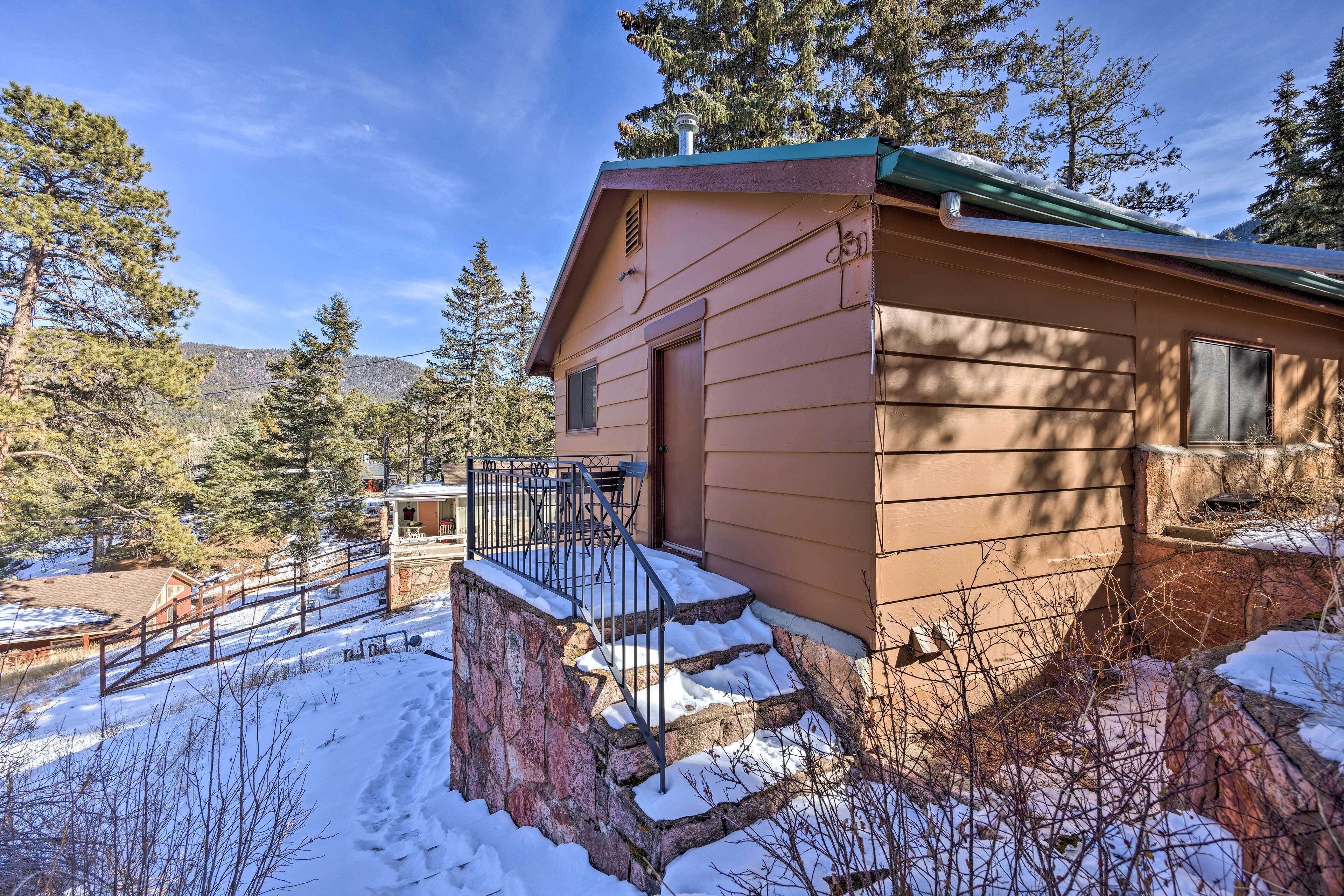 Une cabane avec un escalier en pierre menant à un porche, entourée de neige et d’arbres.