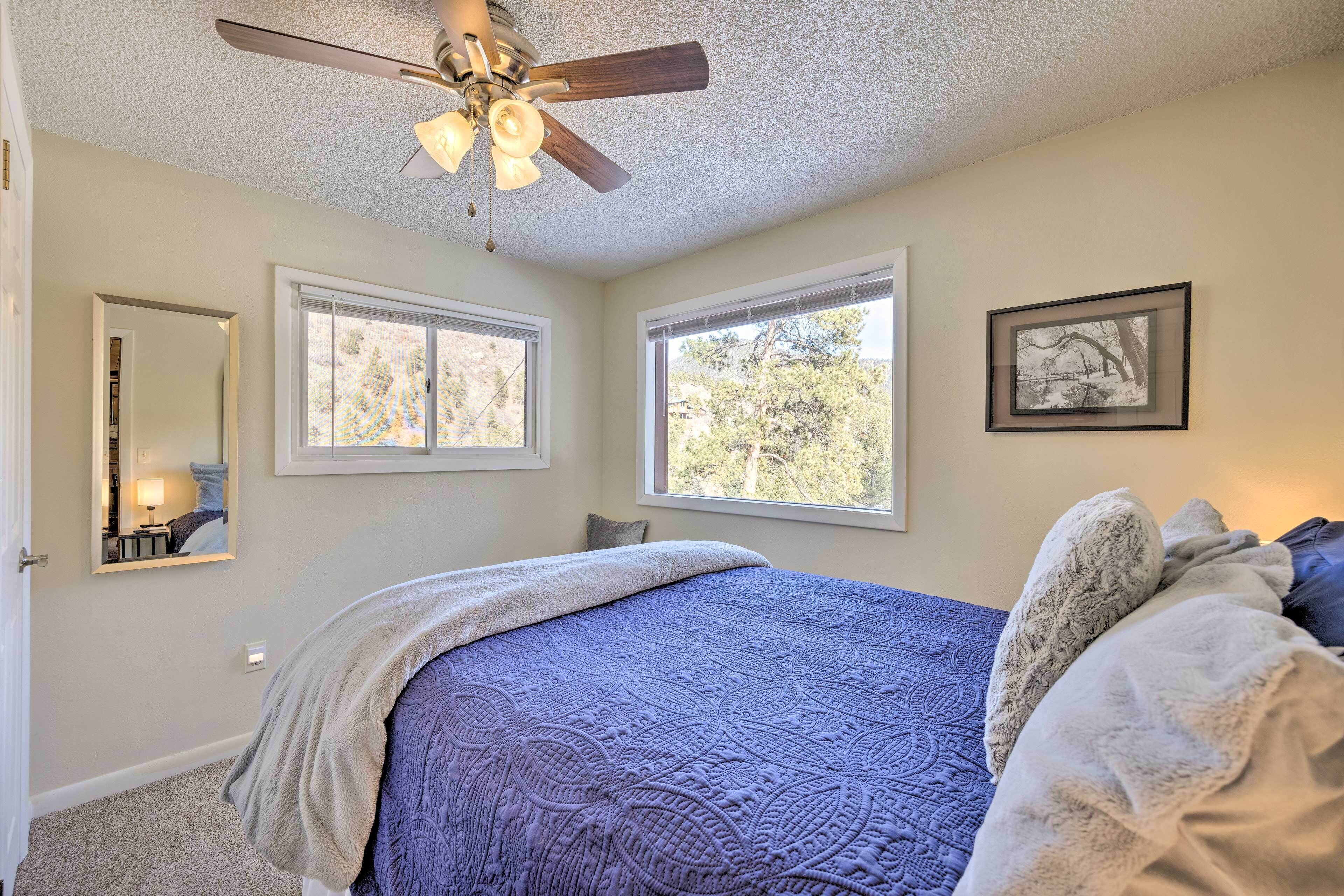 A bedroom with a bed, two windows, a ceiling fan, a framed picture, and a mirror.