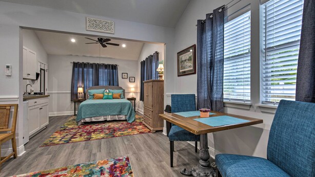 A bedroom with a bed, a desk, and a chair. There is a window with curtains and a ceiling fan.