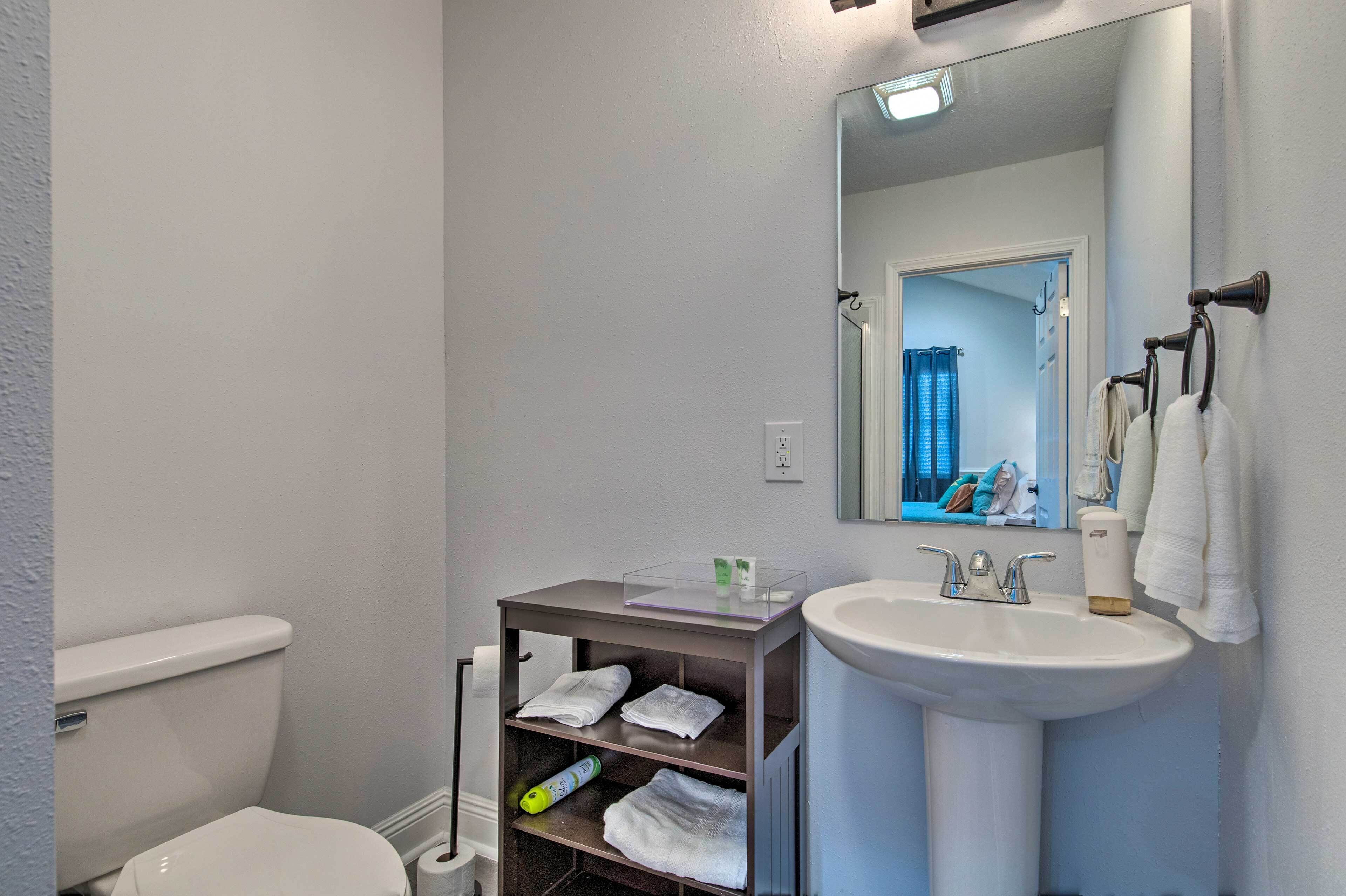 A bathroom with a toilet, a sink, a mirror, and a shelf with towels.