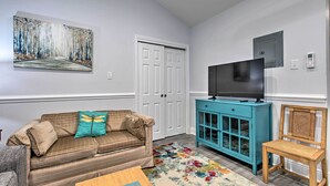 A living room with a sofa, a television on a cabinet, a door, and a wall-mounted artwork.