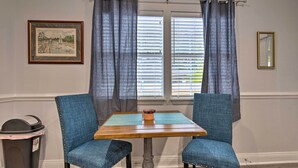 A dining area with a table and two chairs, a trash can, a framed picture, and a mirror on the wall.