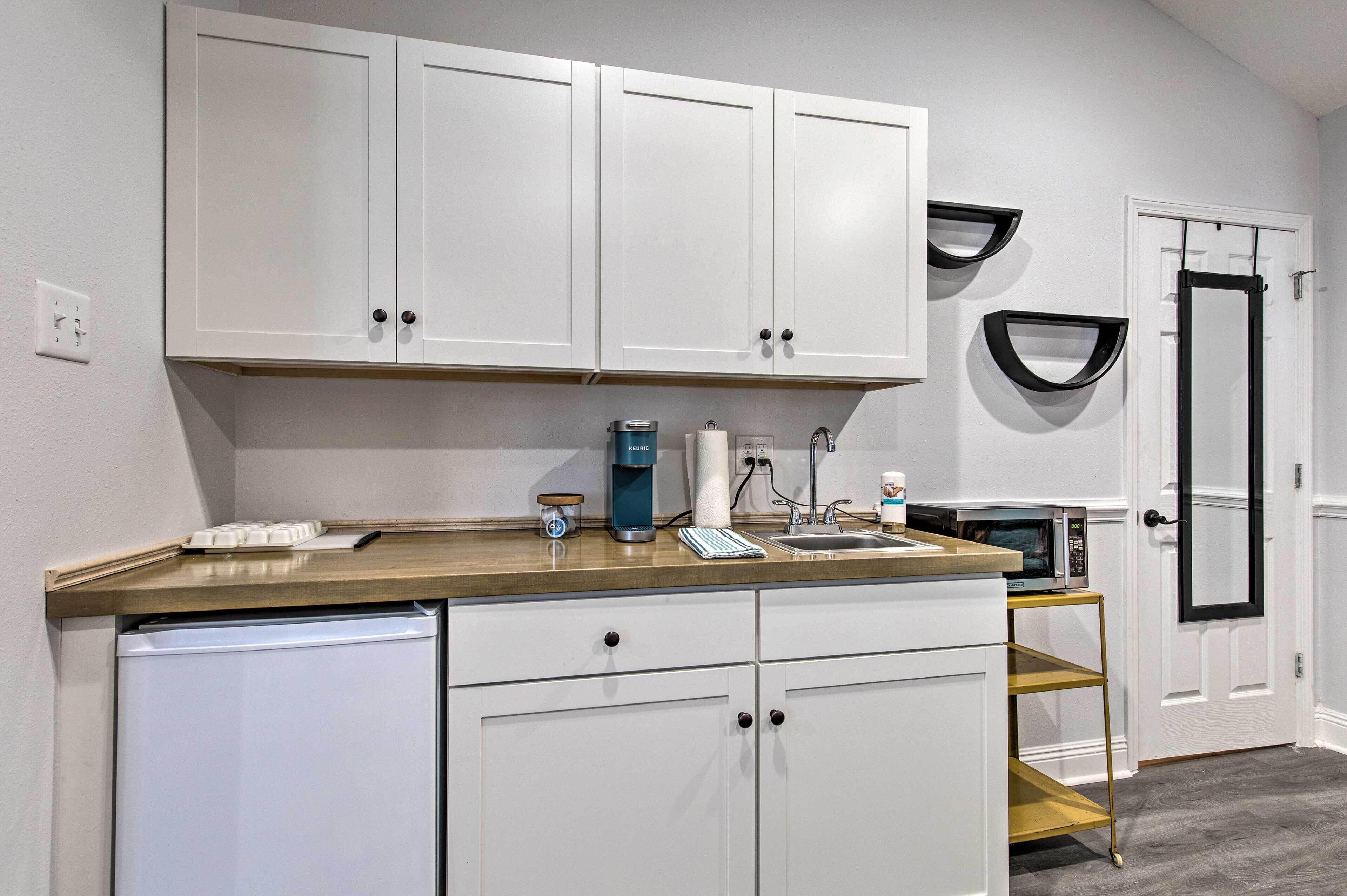 A compact kitchen with white cabinets, a stainless steel sink, and a microwave.