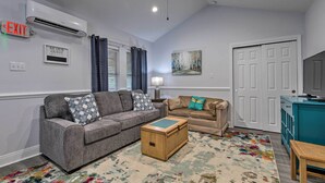 A living room with two sofas, a coffee table, a ceiling fan, an air conditioning unit, and a door.