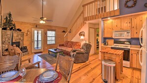 A cozy living room with a fireplace, wooden furniture, a dining area, and a kitchen with wooden cabinets and appliances.