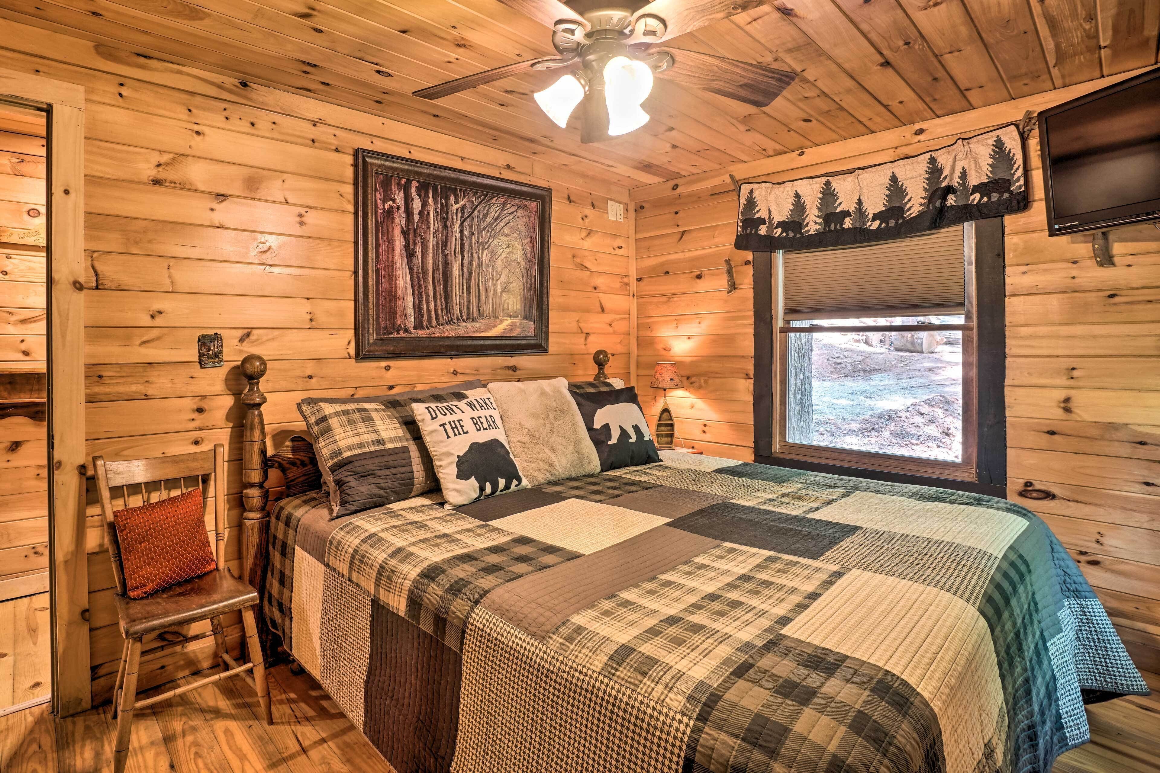 Une chambre confortable, aménagée dans un chalet en bois, avec un lit, une chaise, un ventilateur de plafond, une fenêtre offrant une belle vue et un téléviseur fixé au mur.