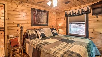 Une chambre confortable, aménagée dans un chalet en bois, avec un lit, une chaise, un ventilateur de plafond, une fenêtre offrant une belle vue et un téléviseur fixé au mur.