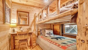 A cozy cabin interior with a bunk bed, a desk with a chair, a mirror, and a window.