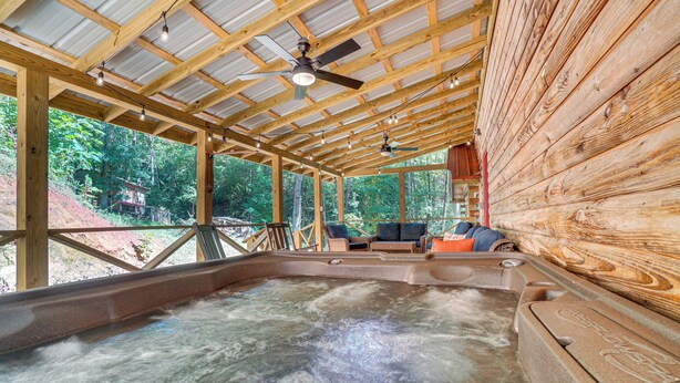 A hot tub area with wooden beams, ceiling fans, and a view of the forest.