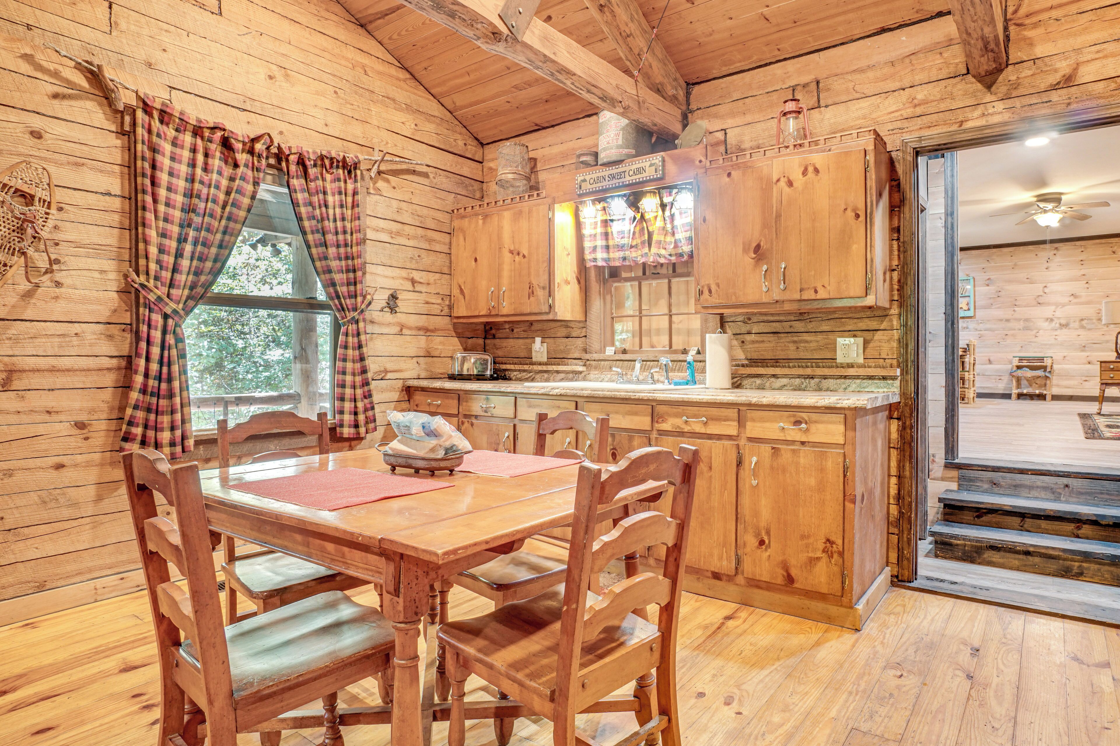 A wooden cabin interior with a dining table, chairs, wooden cabinets, and a kitchen area.