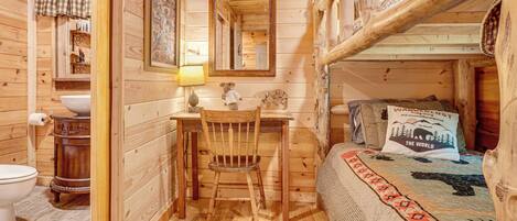 L'intérieur d'une cabane en bois, avec un bureau, une chaise et un lit superposé, tous en bois.