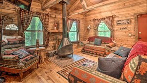 A log cabin interior with a fireplace, wooden furniture, and large windows.