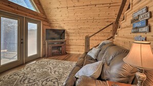 Interior acogedor de una cabaña con techo de madera, sofá de cuero, chimenea y televisor.
