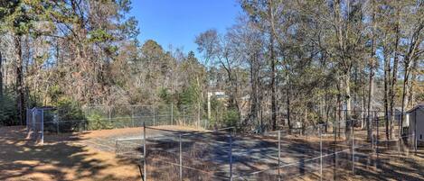 A fenced outdoor area with a metal structure, surrounded by trees and a building in the background.