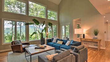 Amplia sala de estar con ventanas grandes, un sofá seccional azul, un sillón de cuero marrón y una mesa de centro.