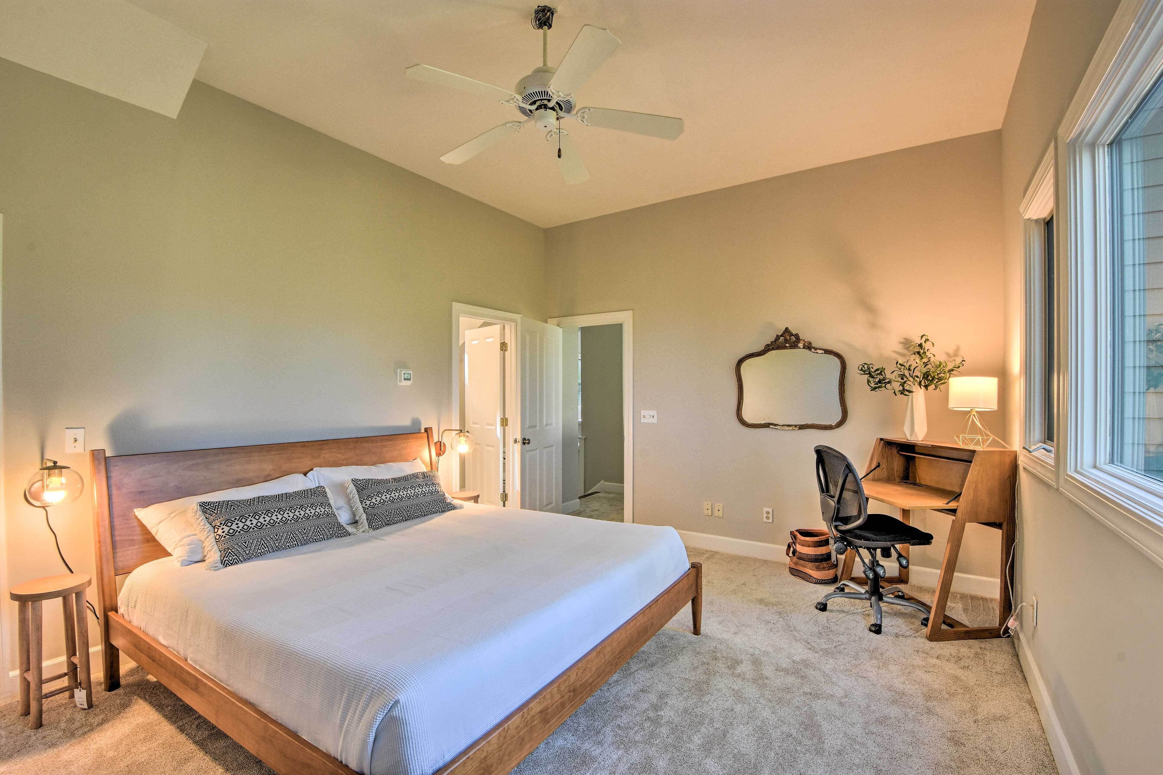A bedroom with a bed, a desk, a chair, a ceiling fan, and a window.