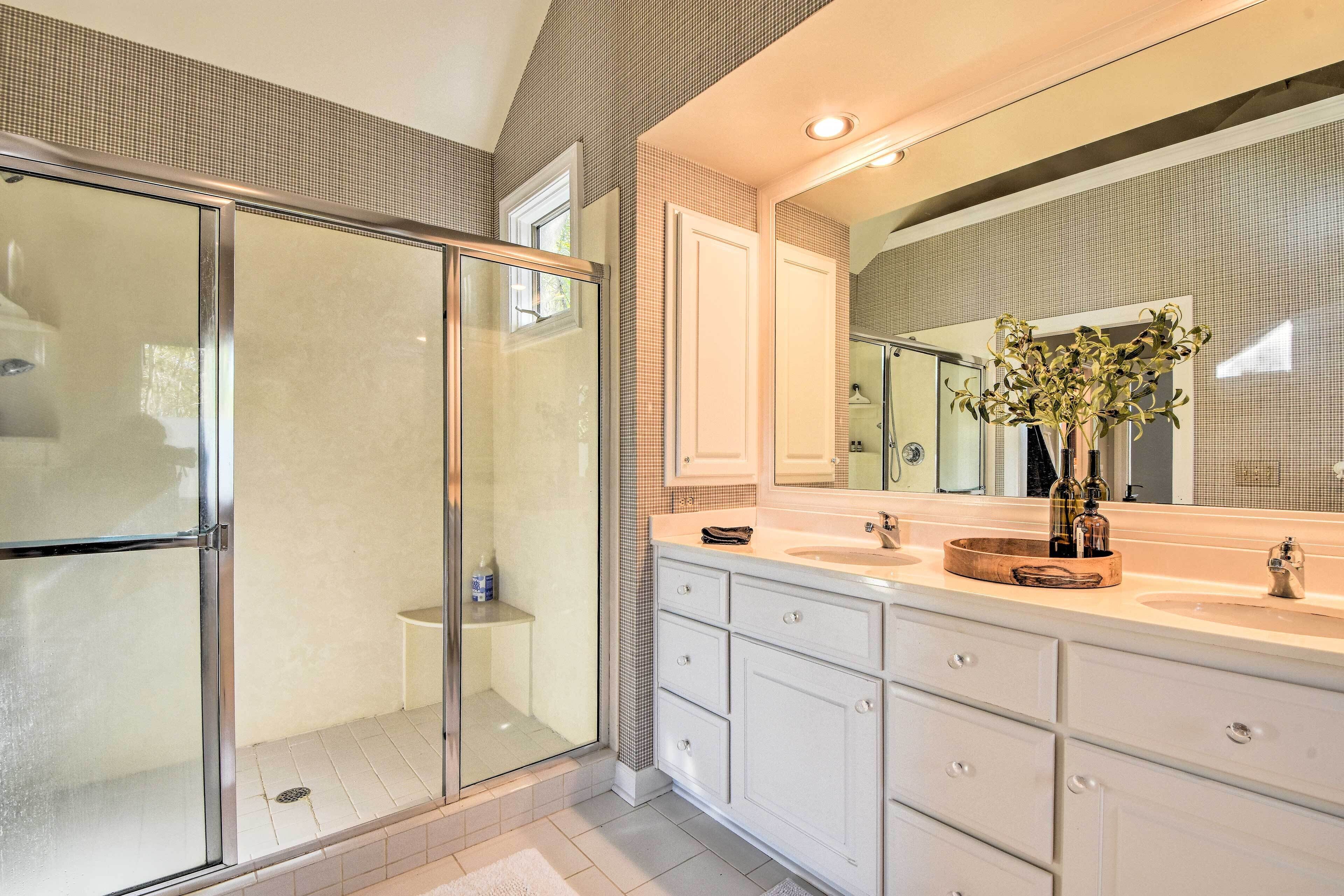 A modern bathroom with a glass shower enclosure, a large mirror, and a vanity with a sink and storage drawers.