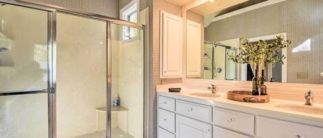 A modern bathroom with a glass shower enclosure, a large mirror, and a vanity with a sink and storage drawers.