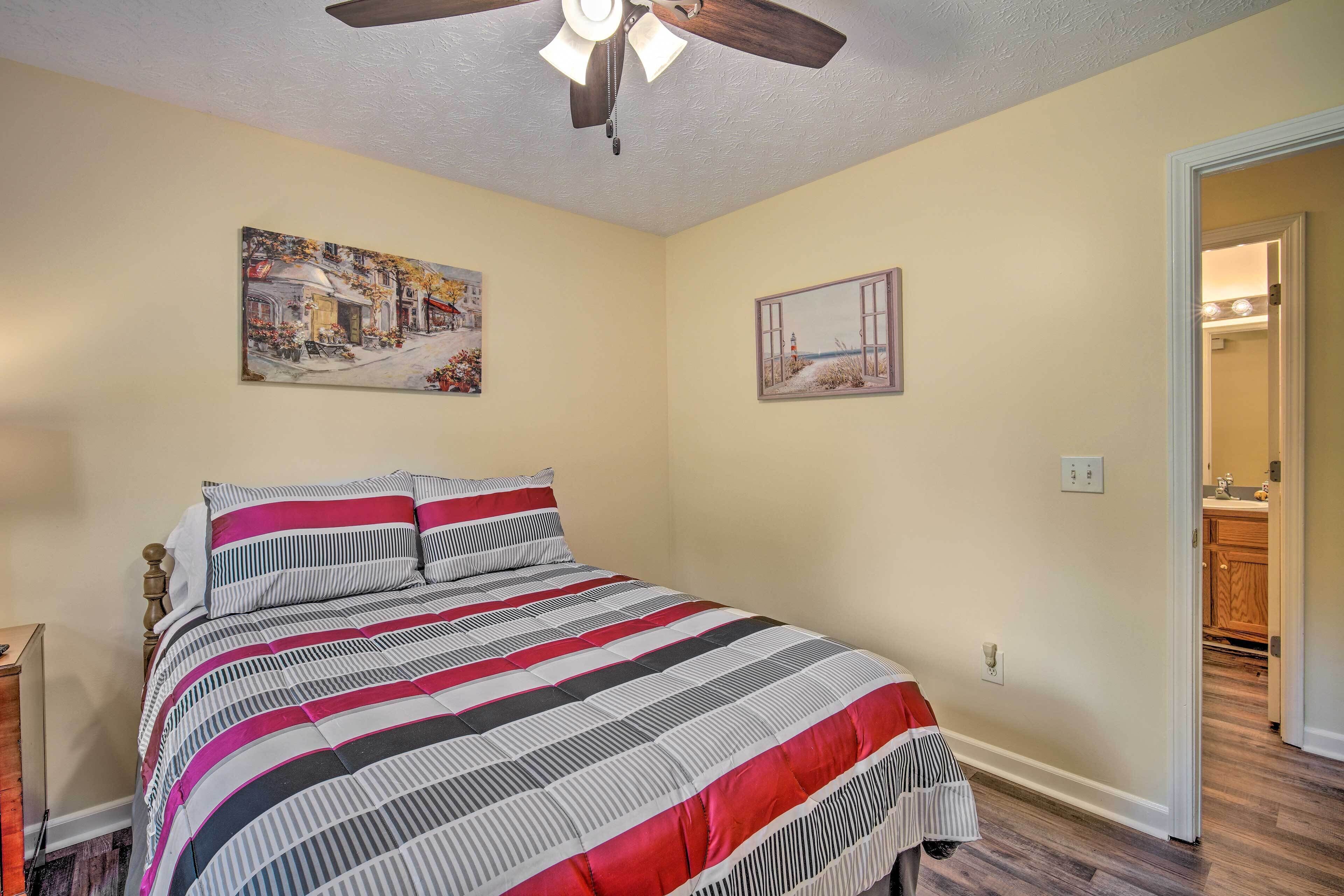 A bedroom with a bed, a ceiling fan, and two wall-mounted paintings.