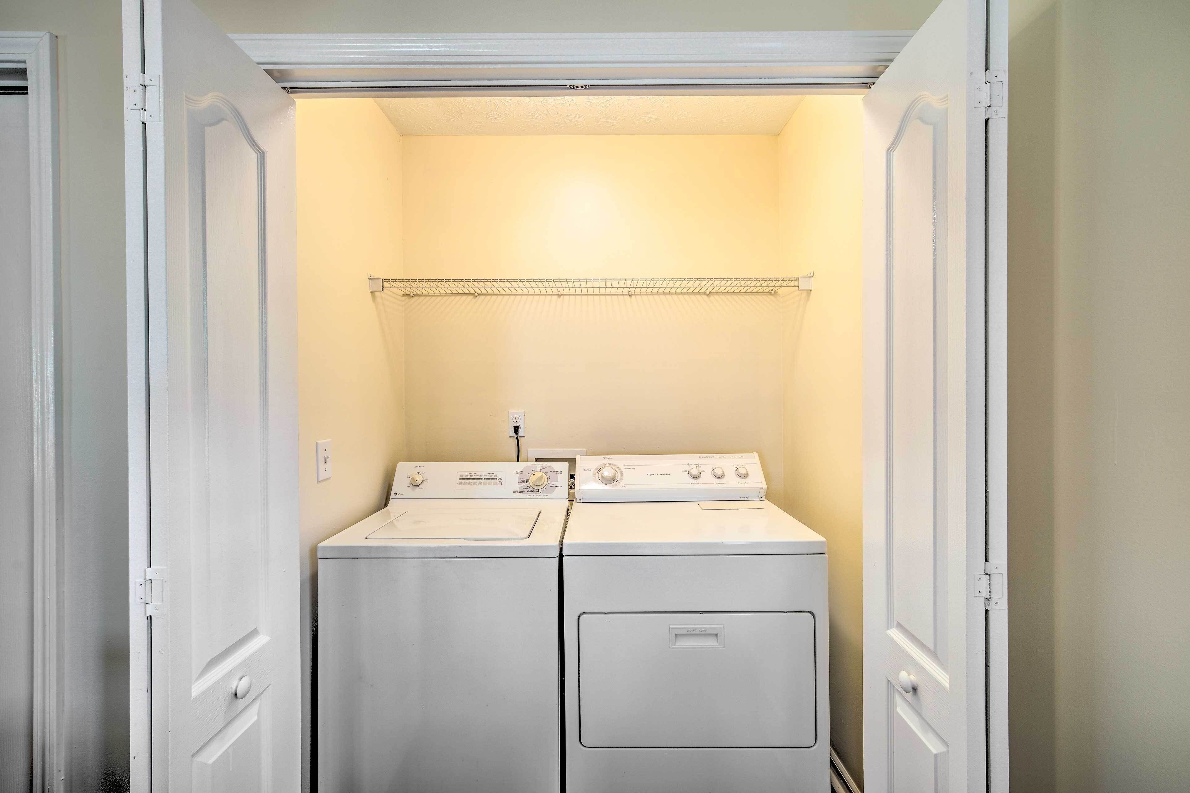 A laundry room with two stacked washers and dryers, a metal drying rack, and a light switch on the wall.
