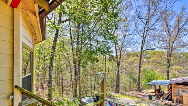 A wooden deck with a railing, a small shed, and a bicycle in a forested area. - Charming Cottage w/ Deck in Blue Ridge! (Blue Ridge)
