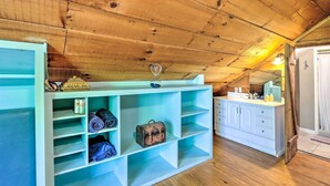 A room with a wooden ceiling, a light blue storage unit with shelves, a small table with a glass, and a bathroom with a mirror and sink. - Charming Cottage w/ Deck in Blue Ridge! (Blue Ridge)