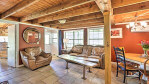 A spacious living area with a wooden ceiling, leather sofas, a dining table with chairs, and large windows allowing natural light. - Charming Cottage w/ Deck in Blue Ridge! (Blue Ridge)