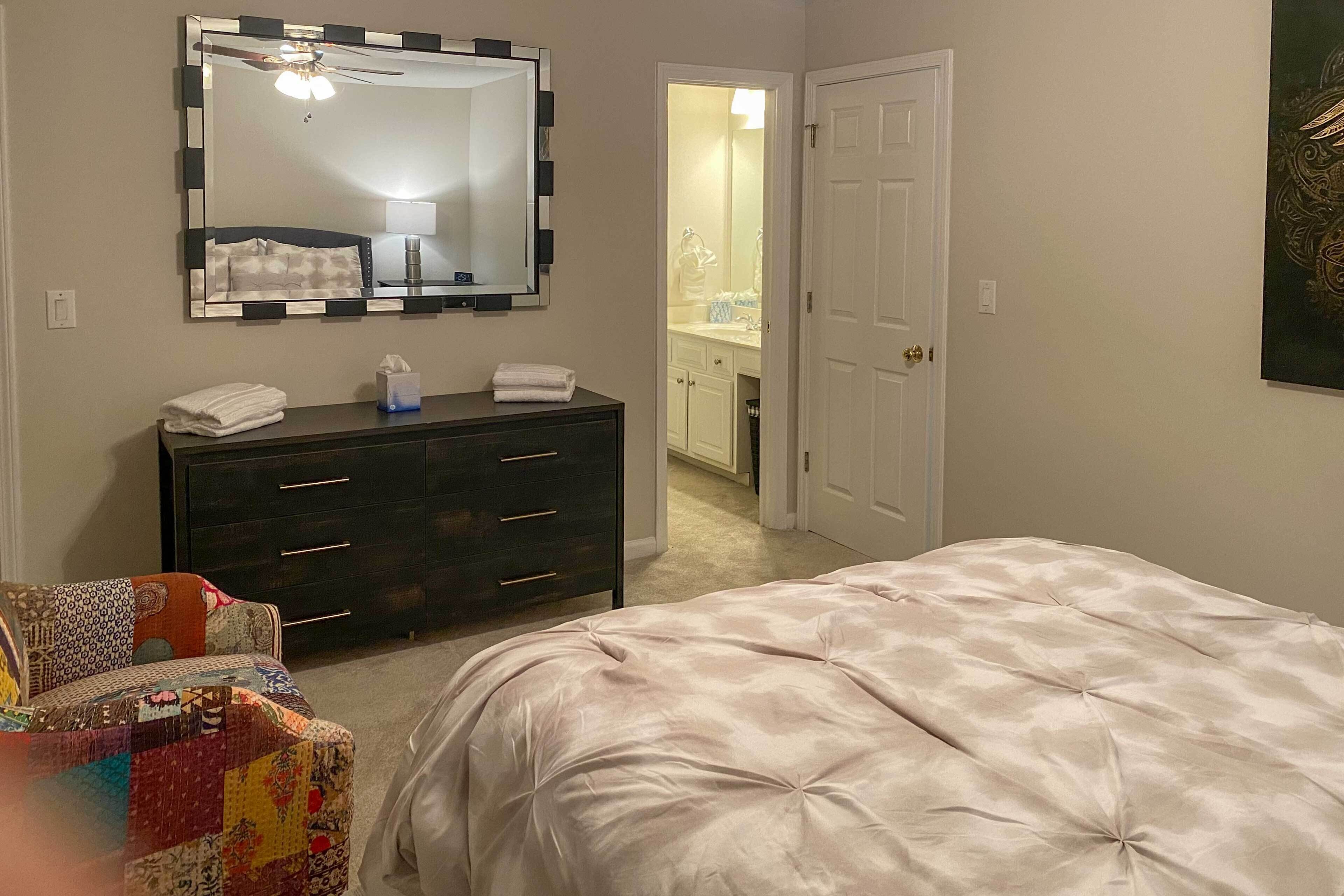 A bedroom with a bed, a dresser, a mirror, and a door leading to a bathroom.