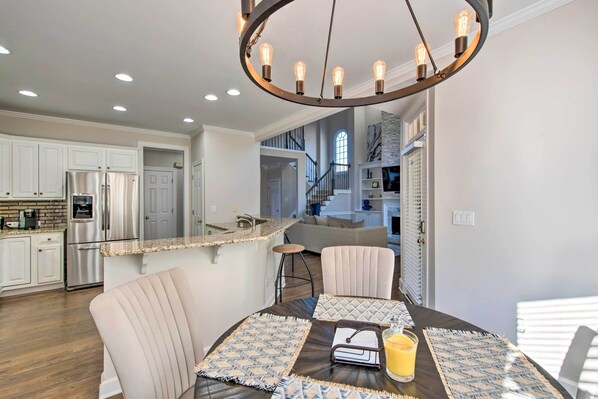 A modern kitchen with stainless steel appliances, a dining area with a round table, and a staircase leading to an upper level. - Updated Mableton Home ~ 14 Miles to Downtown Atl! (Mableton)