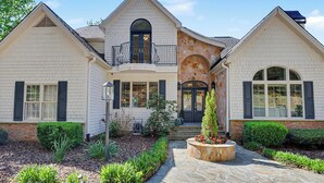 Une maison à deux étages avec une entrée en pierre, un balcon et un jardin bien entretenu.