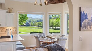 Une cuisine avec un mur recouvert de pierres, un coin repas avec une table dressée pour quatre personnes, et de grandes fenêtres offrant une vue sur un paysage verdoyant.