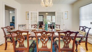 A dining room with a chandelier, wooden chairs, a glass-top table, and a framed picture on the wall. - Main Street Home: 1 Mi to Callaway Gardens (Pine Mountain)