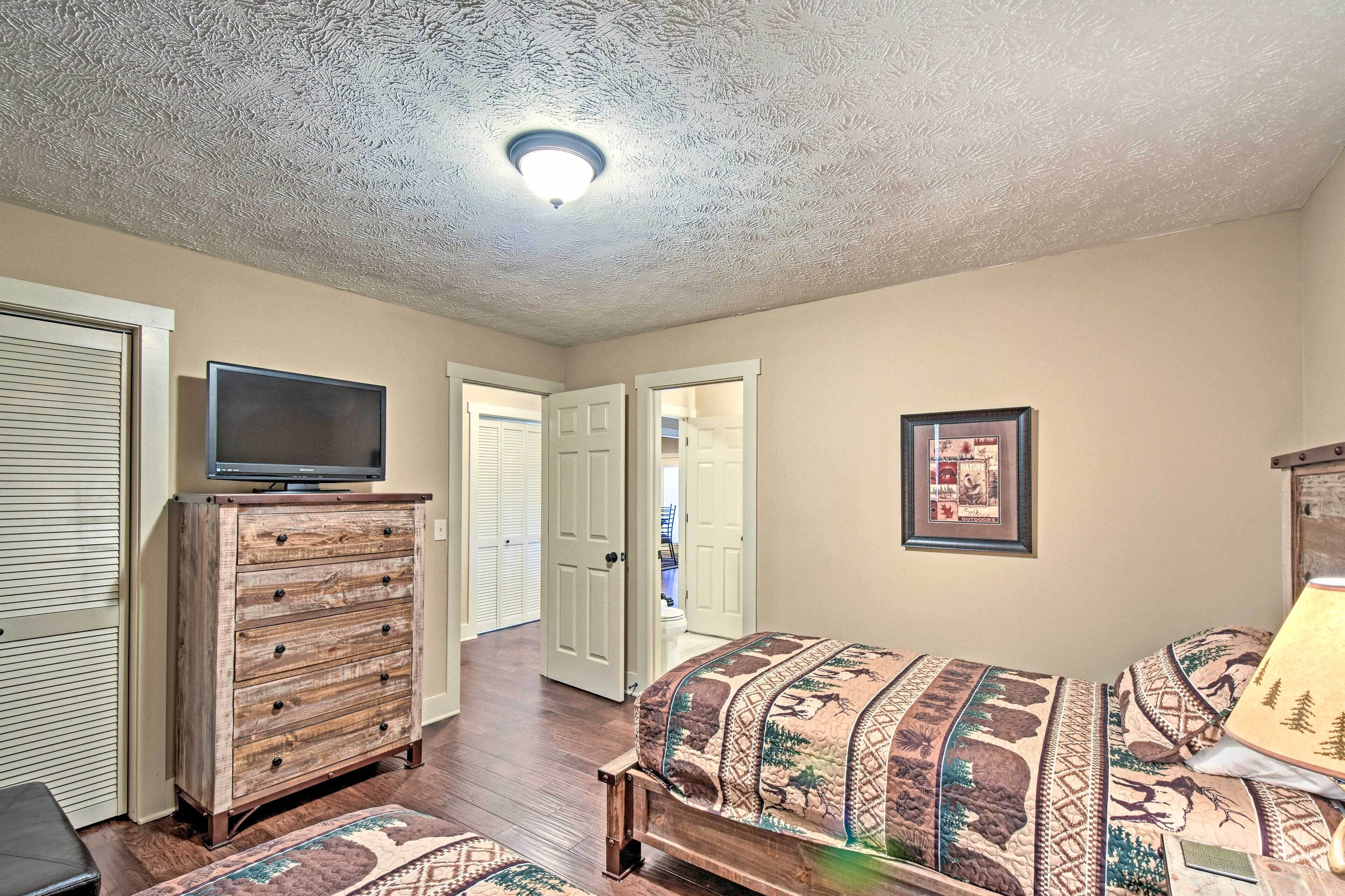A bedroom with a wooden dresser, a bed with patterned bedding, a television on the dresser, and a framed picture on the wall.