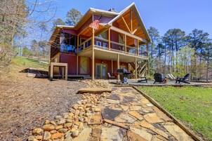 A two-story wooden cabin with a porch, stone pathway, and outdoor seating area.