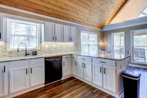 A kitchen with white cabinets, a dishwasher, and a black trash can. - Sparta Home w/ On-site Lake Access! (Milledgeville)