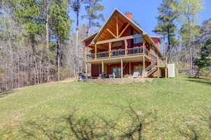A two-story log cabin with a balcony, surrounded by a forest.